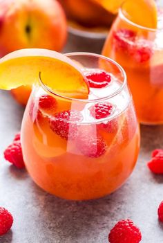 two glasses filled with liquid and topped with raspberries next to sliced peaches