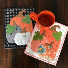 two place mats with pumpkins and leaves on them, one has a cup holder