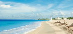 the woman is walking down the beach towards the water and lounge chairs on the sand