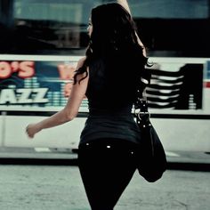 a woman walking down the street in front of a bus with her back to the camera