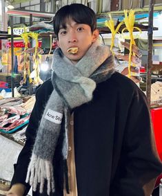 a young man wearing a scarf and eating food in a market area with other items