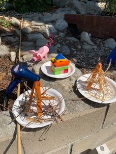 three paper plates with sticks sticking out of them sitting on a cement ledge next to rocks and plants