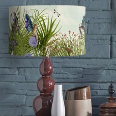 three vases and a lamp on a table in front of a blue brick wall