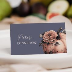 a place card sitting on top of a white plate with fruit in the back ground