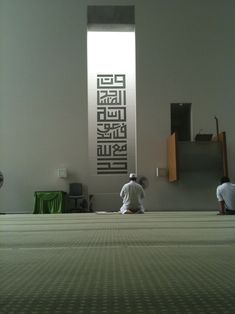 two men kneeling down in front of a wall with arabic writing on it and another man standing next to the wall