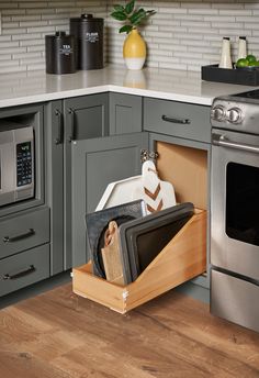 an open drawer in the middle of a kitchen with gray cabinets and stainless steel appliances