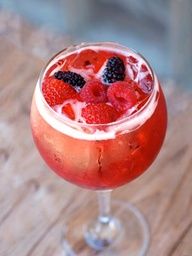 a close up of a drink in a glass on a wooden table with berries and ice