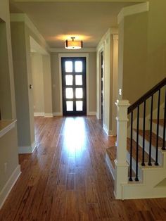 an empty hallway with wooden floors and white railings on either side, leading to the front door