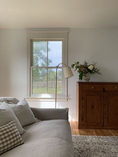 a living room filled with furniture and a lamp on top of a wooden dresser next to a window