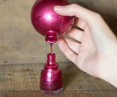 a hand holding a red nail polish bottle with it's top on the table