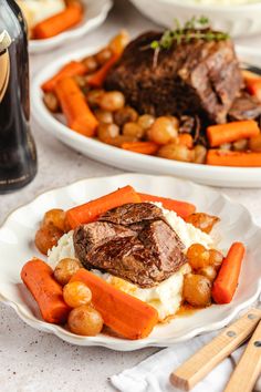 two plates with meat, mashed potatoes and carrots next to a bottle of booze