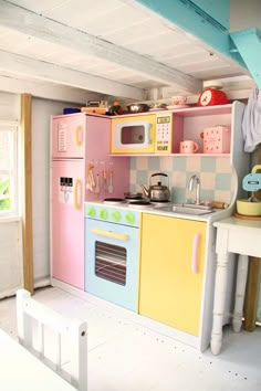 a child's play kitchen with pink, yellow and blue appliances