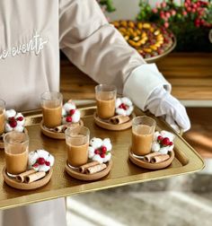 a person is holding a tray with desserts on it and cups in front of them