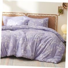 a bed with purple comforter and pillows on it in a room next to a lamp