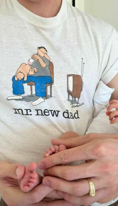 a man sitting in a chair with his hand on the baby's thumb while he is holding it