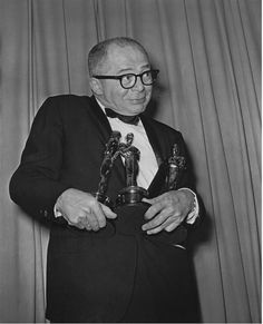 an older man in a tuxedo holding two oscars