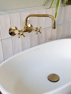 a bathroom sink with gold faucet and white tile wall behind it, next to a potted plant