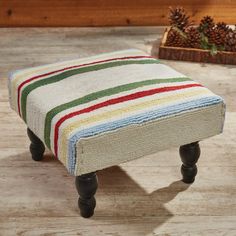 a striped foot stool sitting on top of a wooden floor next to a pine cone