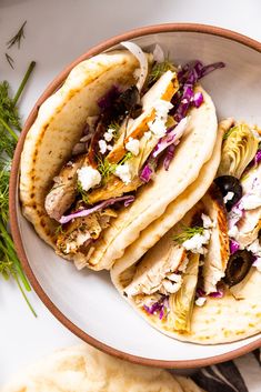 three pita breads with olives, feta cheese and herbs in a bowl