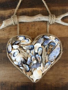 a heart made out of seashells hanging from a rope on a wooden wall