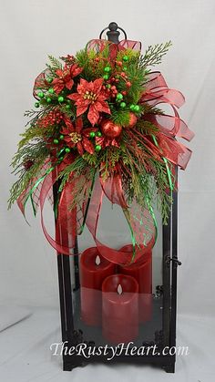 a red candle is sitting in front of a lantern with poinsettia and greenery