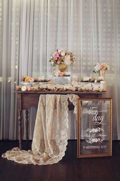 a table topped with a sign and flowers next to a window covered in sheer curtains