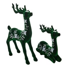 two green deer figurines with white flowers and leaves on their antlers, one is standing next to the other