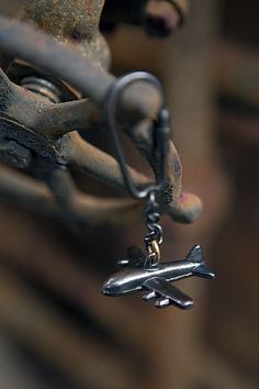 an airplane charm hanging from the side of a piece of metal with a chain attached to it