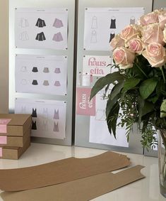 flowers in a vase on a table next to boxes and paper with clothes cut out