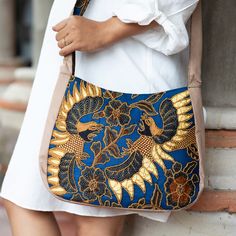 Sawunggaling refers to a traditional Javanese pattern inspired by the King's favorite rooster, a symbol of the nation's power and beauty. Featured in many complexes, this captivating image is now present in Wahyu Sulistiani's cotton shoulder bag, crafted using batik techniques. The accessory comes in a blue hue, with golden-toned plastic beads adding an elegant touch. On top of that, the design has a zippered closure, a black cotton lining and an interior pocket. Unique Pottery, Buy Bead, Plastic Beads, Blue Hues, Handbag Accessories, Black Cotton, Batik, Rooster, Outfit Accessories