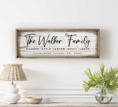 a wooden sign hanging on the wall above a table next to a lamp and potted plant