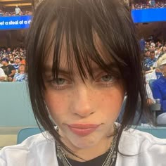 a woman with black hair wearing a white shirt at a baseball game looking into the camera