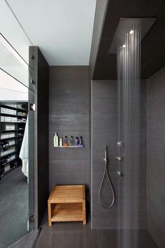 a bathroom with a shower head, wooden stool and shelves on the wall next to it