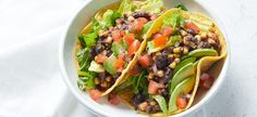 two tacos with lettuce, tomatoes and black beans in a white bowl