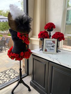 a mannequin with red flowers and a hat on it in front of a window