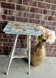 a small table with flowers in a vase next to it on the ground near a brick wall