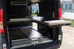 the back end of a black van with its doors open and two trays on it