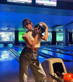 a woman holding a bowling ball in her right hand while standing next to some bowling lanes