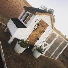 a small white house sitting on top of a dirt field next to a brick wall