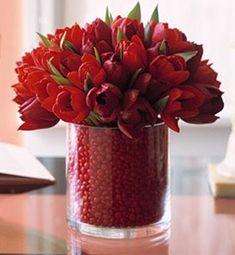 a vase with red flowers sitting on a table next to a lamp and open book