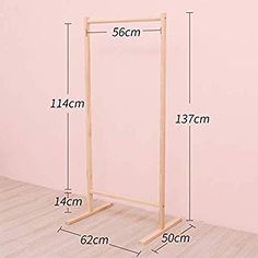 the measurements for a wooden clothes rack in front of a pink wall with wood flooring