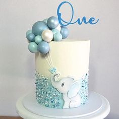 a blue and white cake with an elephant on it's side, surrounded by balloons