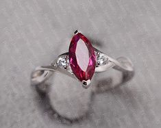 a white gold ring with an oval shaped ruby and diamond set in the center, on a gray surface