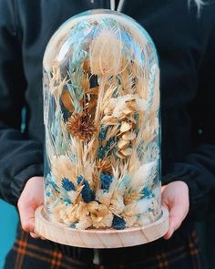 a person holding a glass dome with dried flowers in it