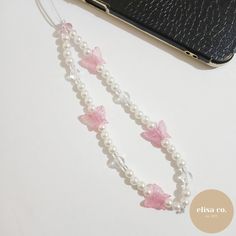 two bracelets with pink bows and pearls are next to a cell phone on a table