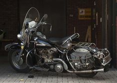 a black motorcycle parked in front of a brick building next to a sidewalk and door