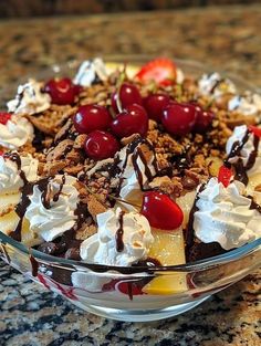 a dessert with cherries and whipped cream in a glass bowl on a granite counter