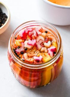 a glass jar filled with food next to two bowls full of beans and other foods