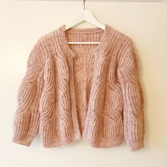 a pink cardigan sweater hanging on a white hanger next to a light colored wall