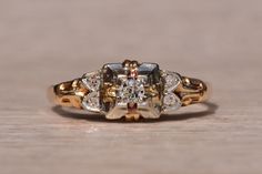 an antique diamond ring is shown on a wooden surface, with the center stone surrounded by smaller diamonds